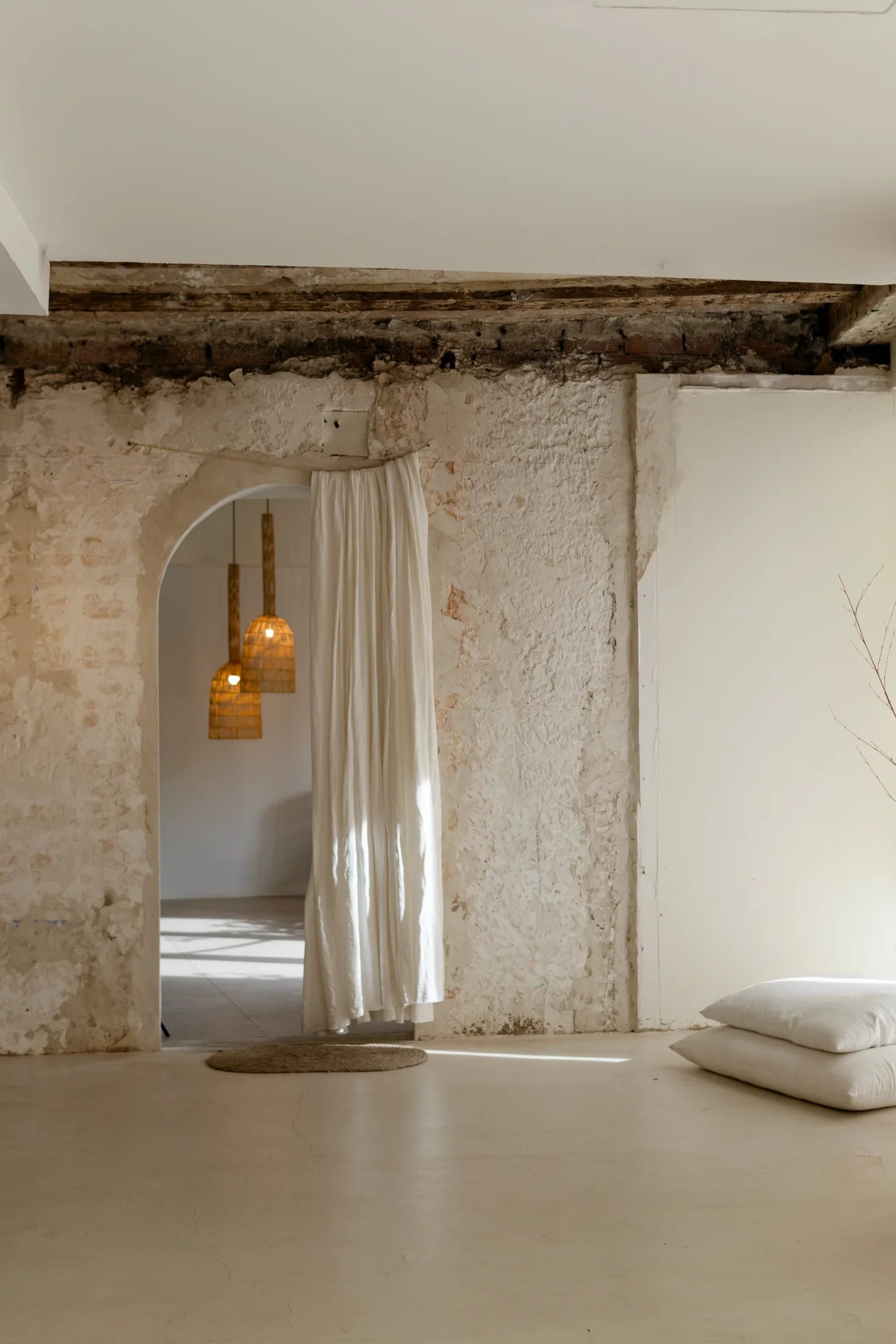 Interior de OASIS con paredes de piedra, cortinas blancas y lámparas colgantes de fibras naturales.