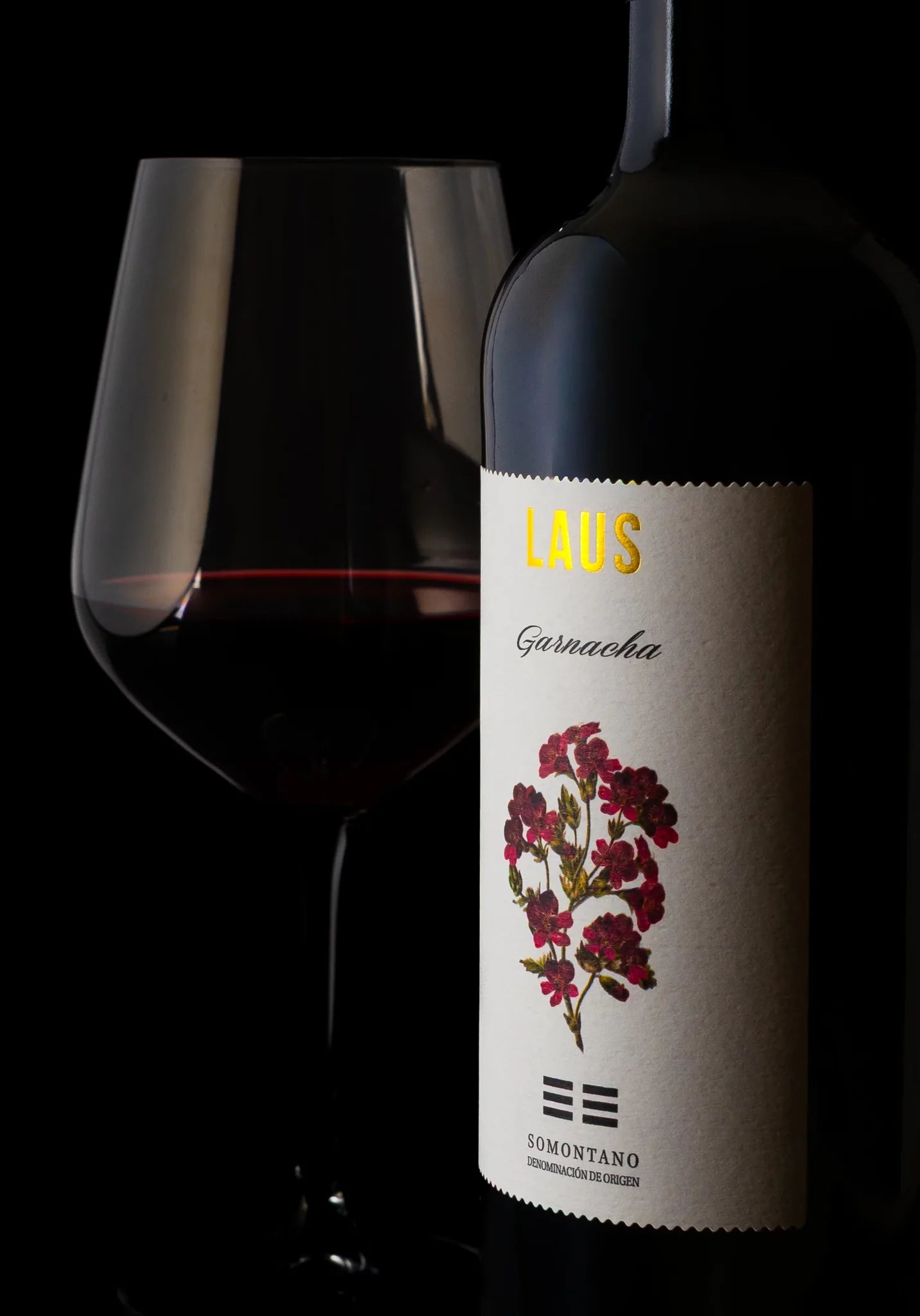 Botella de vino tinto LAUS y copa sobre fondo negro.